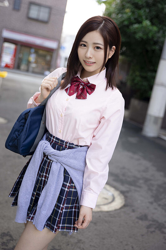 屋外で制服風の衣装を着て、腰にカーディガンを巻きながらこちらを見る女性の全身カット